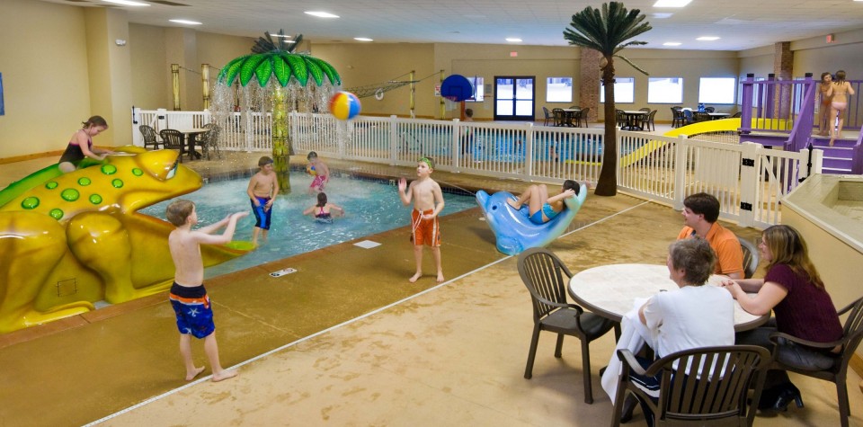 Children playing in waterpark area with a frog slide, and palm tree waterfall